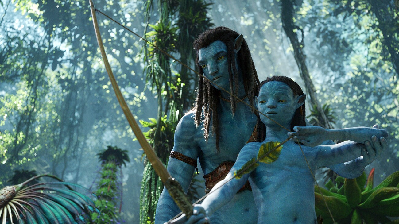 Avatar: The Way of Water (2022): Jake Sully guides young Neteyam as he holds a bow in Pandora’s green forest