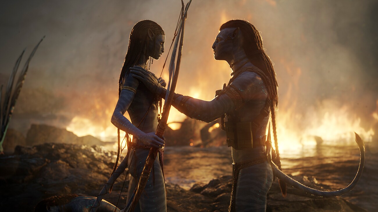 Avatar: The Way of Water (2022): Jake holds Neytiri’s shoulders as they face each other with burning forest visible behind them