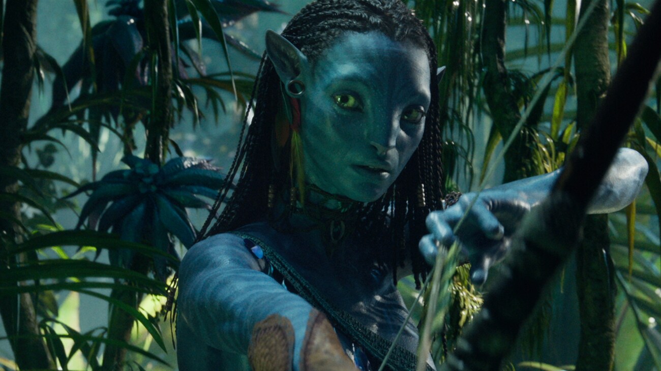 Avatar: The Way of Water (2022): Neytiri draws her bow among hanging vines and green leaves in Pandora’s forest