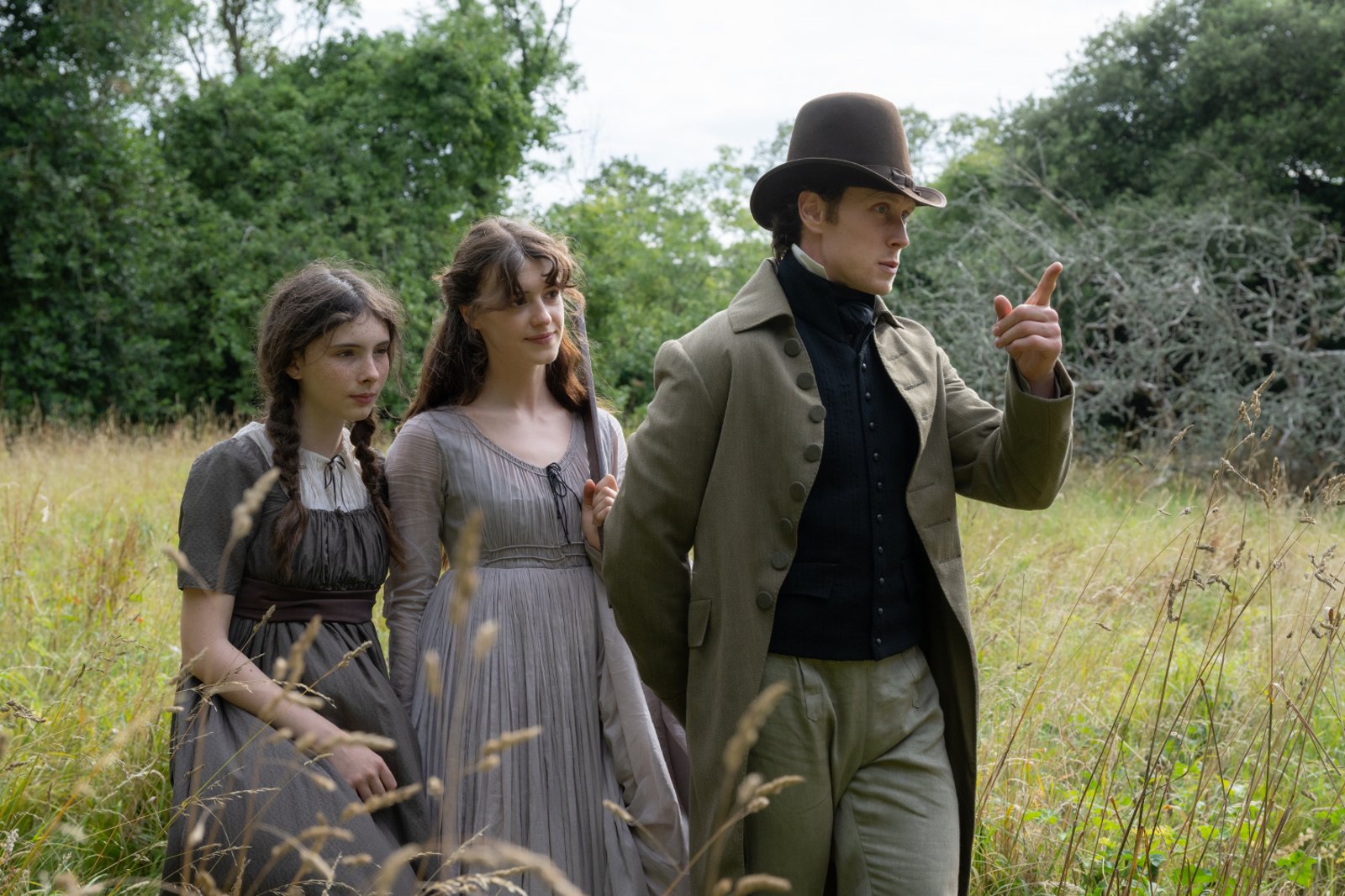 Sense and Sensibility (2026) — Margaret, Elinor and Edward outdoors Sense and Sensibility (2026): Bodhi Rae Breathnach and Daisy Edgar-Jones stand in a grassy field beside George MacKay, who gestures while wearing a top hat