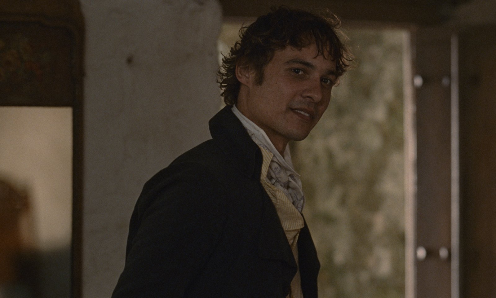 Sense and Sensibility (2026) — Frank Dillane as Willoughby Sense and Sensibility (2026): Frank Dillane as John Willoughby turns toward the camera in a dark coat beside an open doorway