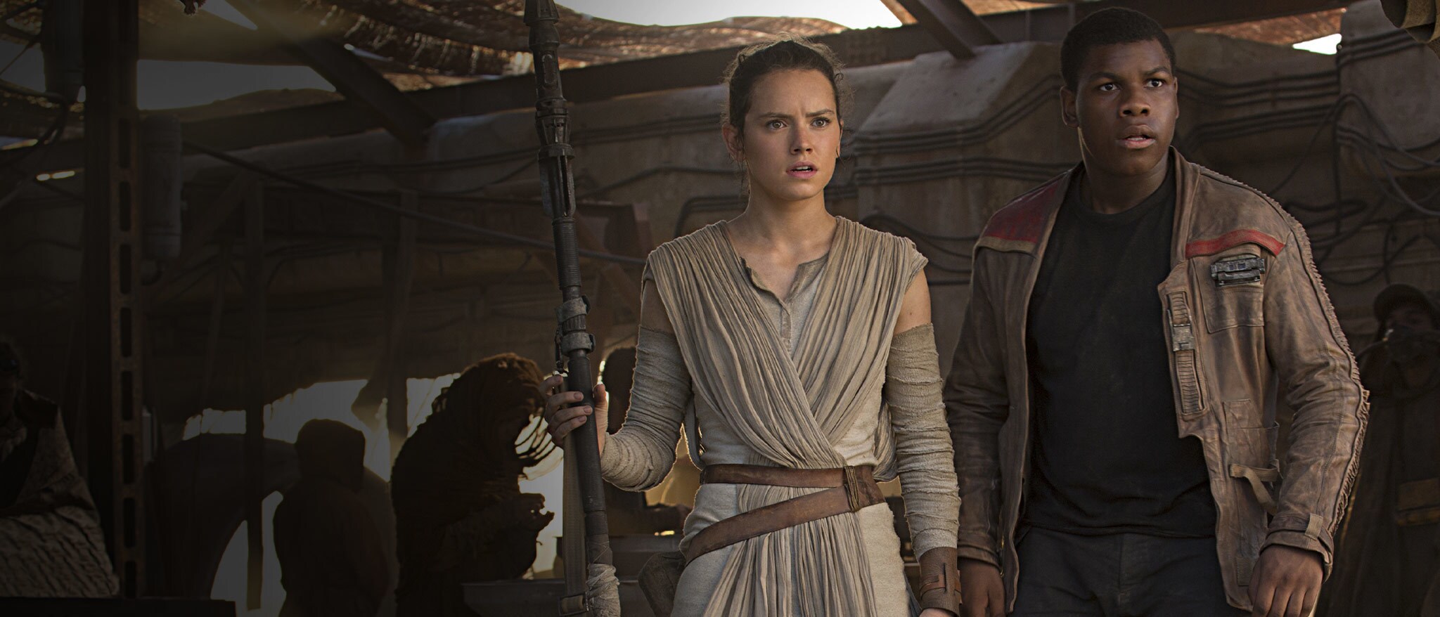Star Wars: The Force Awakens (2015) — Rey and Finn stand together on Jakku Star Wars: The Force Awakens (2015): Rey holds her staff beside Finn beneath the shade of a market shelter