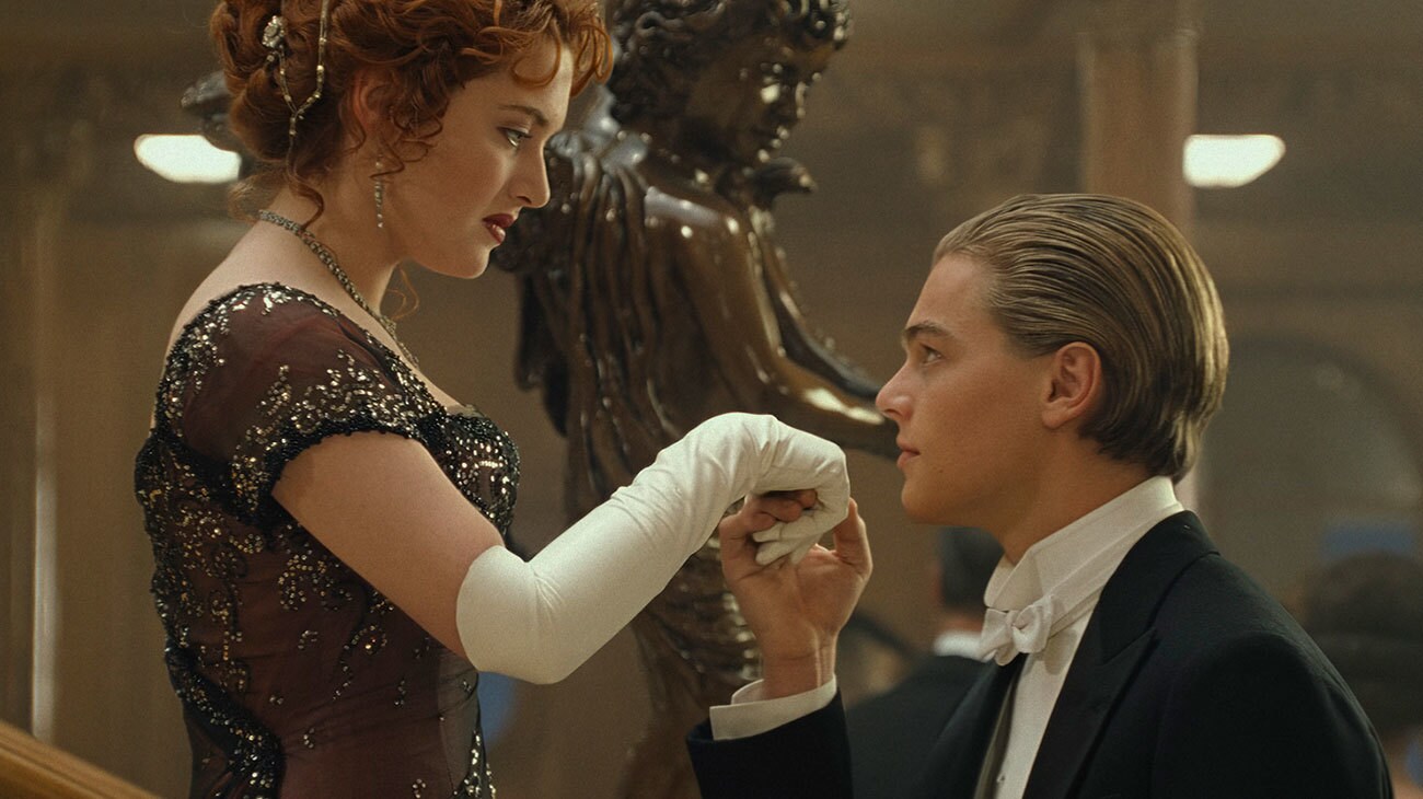 Titanic (1997) — Jack greets Rose in formal evening dress Titanic (1997): Jack in black formalwear kisses Rose’s white-gloved hand beside an ornate staircase