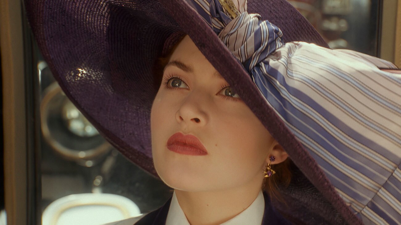 Titanic (1997) — Rose arrives beneath her wide-brimmed hat Titanic (1997): Rose looks upward beneath a wide purple hat decorated with a striped bow