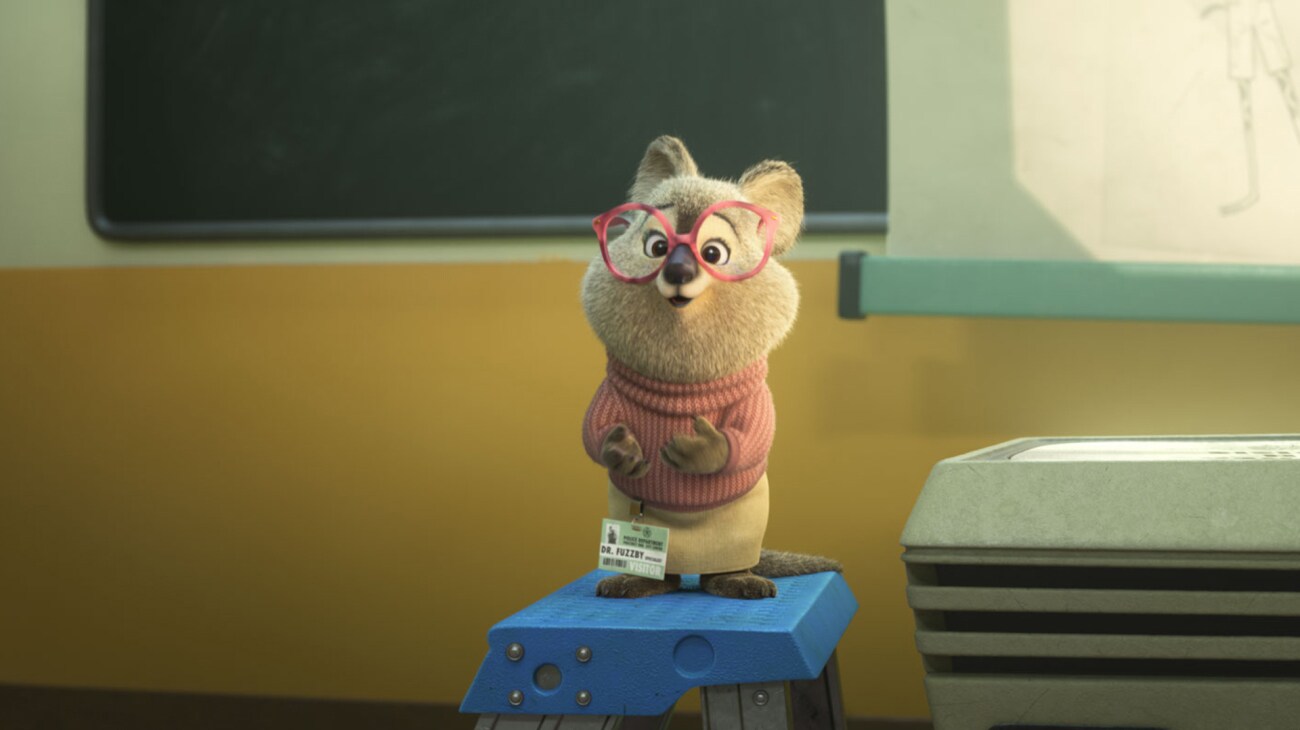 Zootopia 2 (2025) — Dr. Fuzzby brings partnership into the classroom Zootopia 2 (2025): Dr. Fuzzby wears large pink glasses and stands on a blue stool in front of a classroom chalkboard
